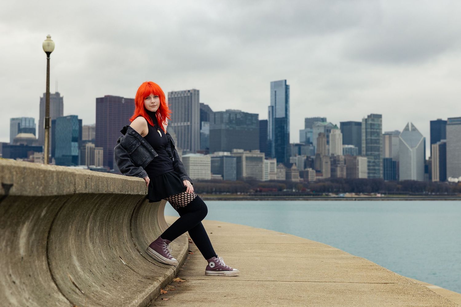 Red-haired woman in black outfit posing on a pier with Chicago skyline in the background.