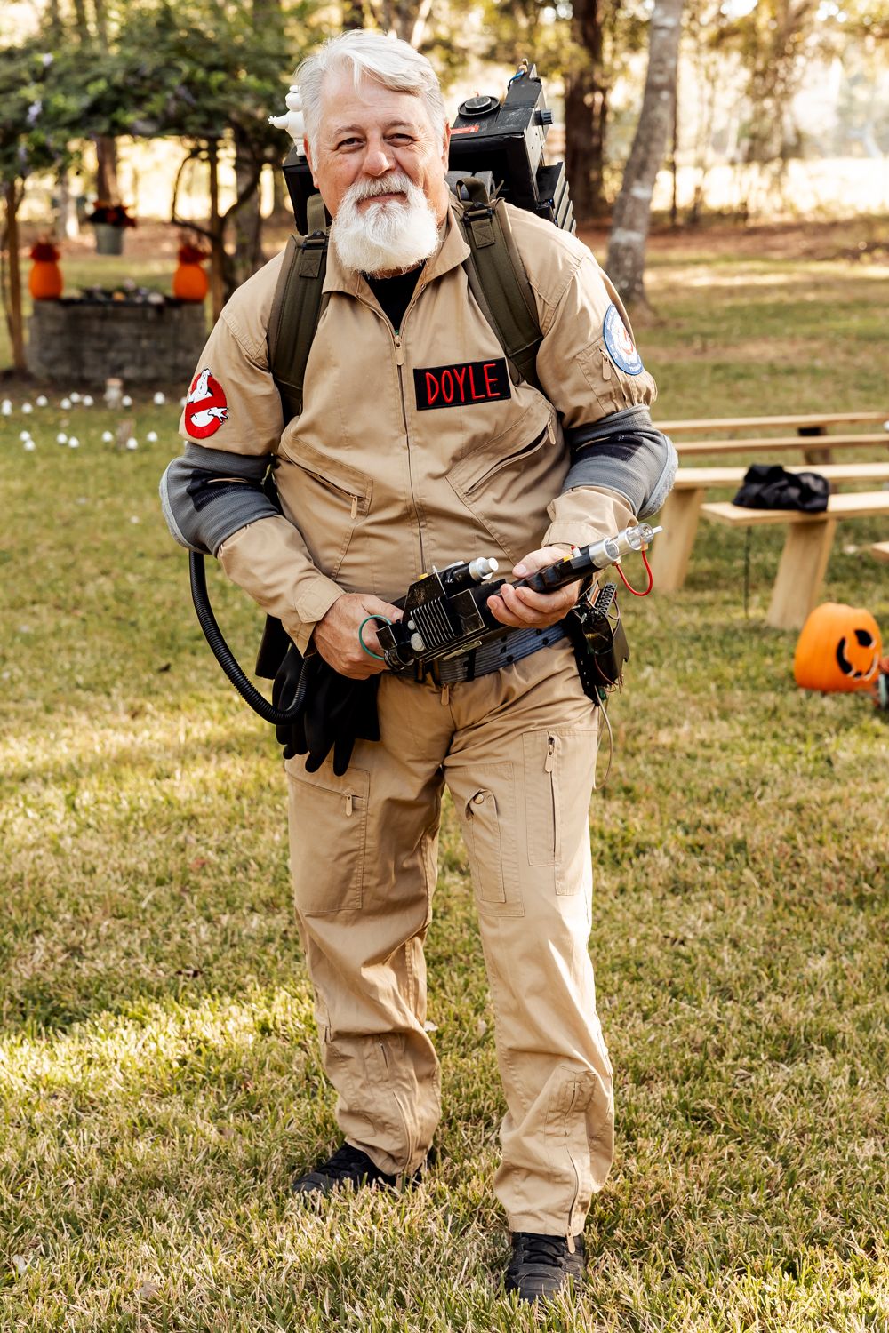 A photographer in beige tactical gear carries professional camera equipment outdoors.