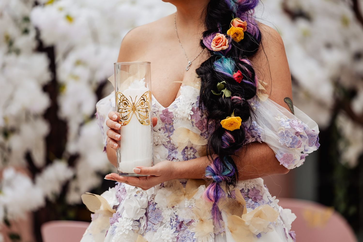 Bride in floral purple gown holds butterfly champagne flute with colorful flowers braided in dark hair.