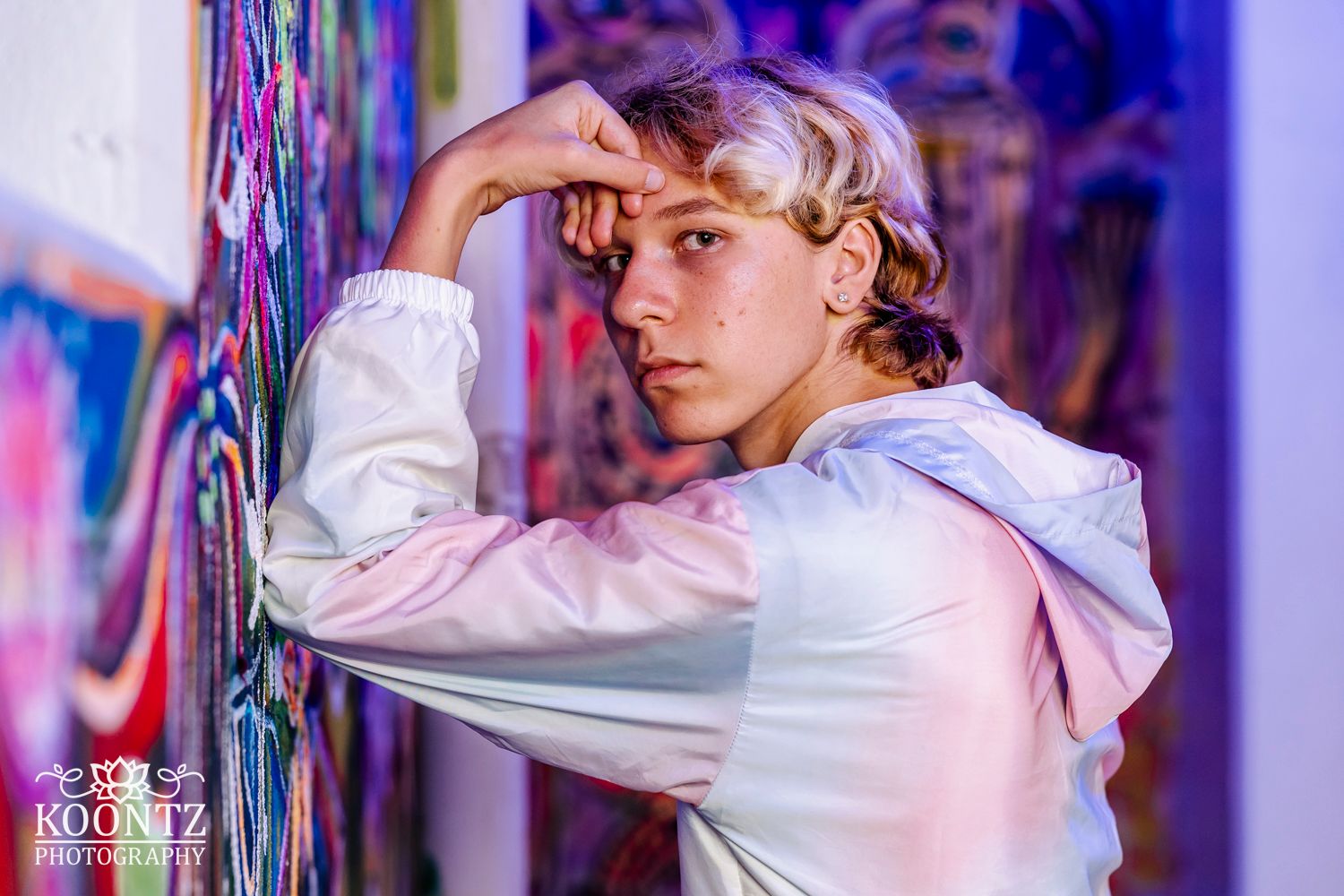 Artistic photo of a person in a white hoodie posing against vibrant purple graffiti wall.