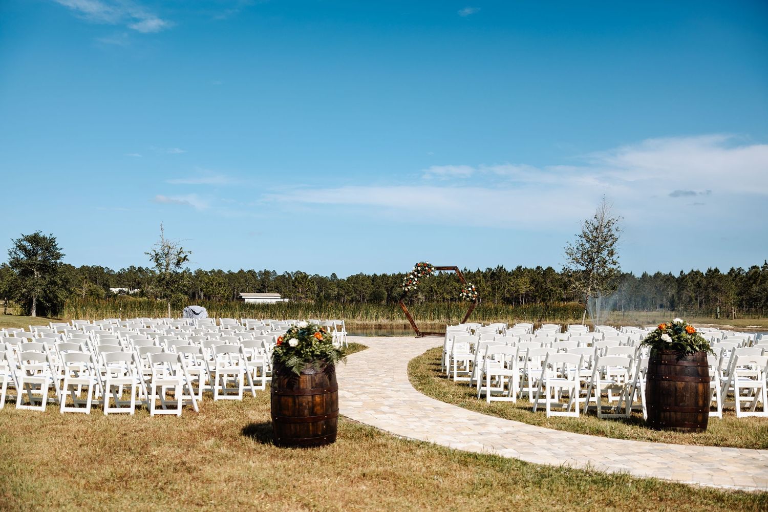 White ceremony chairs lined up along a curved path for an outdoor wedding.