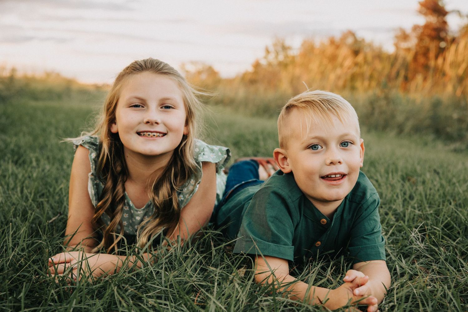 Two playful children lying in green grass during golden hour at sunset.