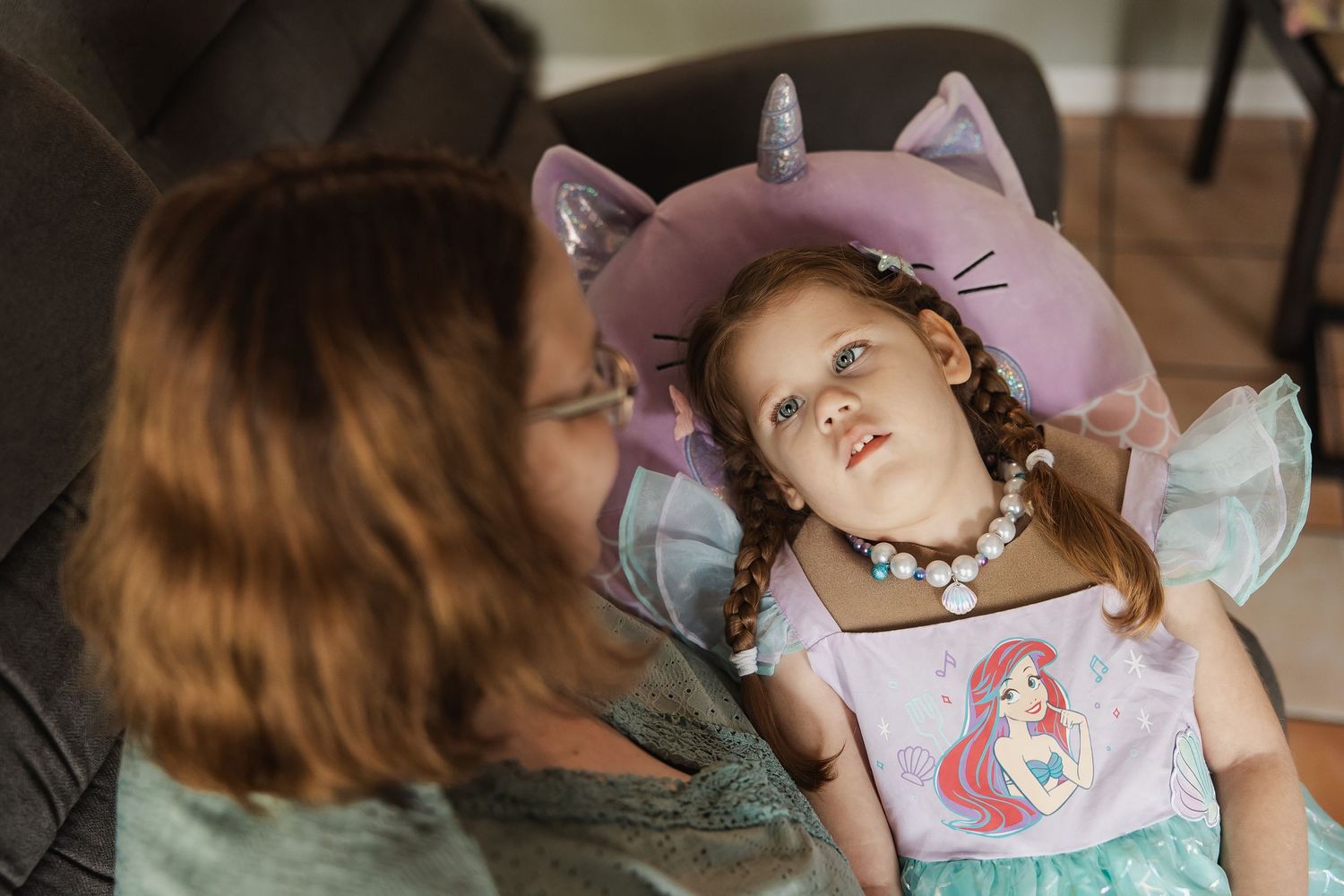 Woman looking at a young girl dressed in a mermaid costume with unicorn pillow.