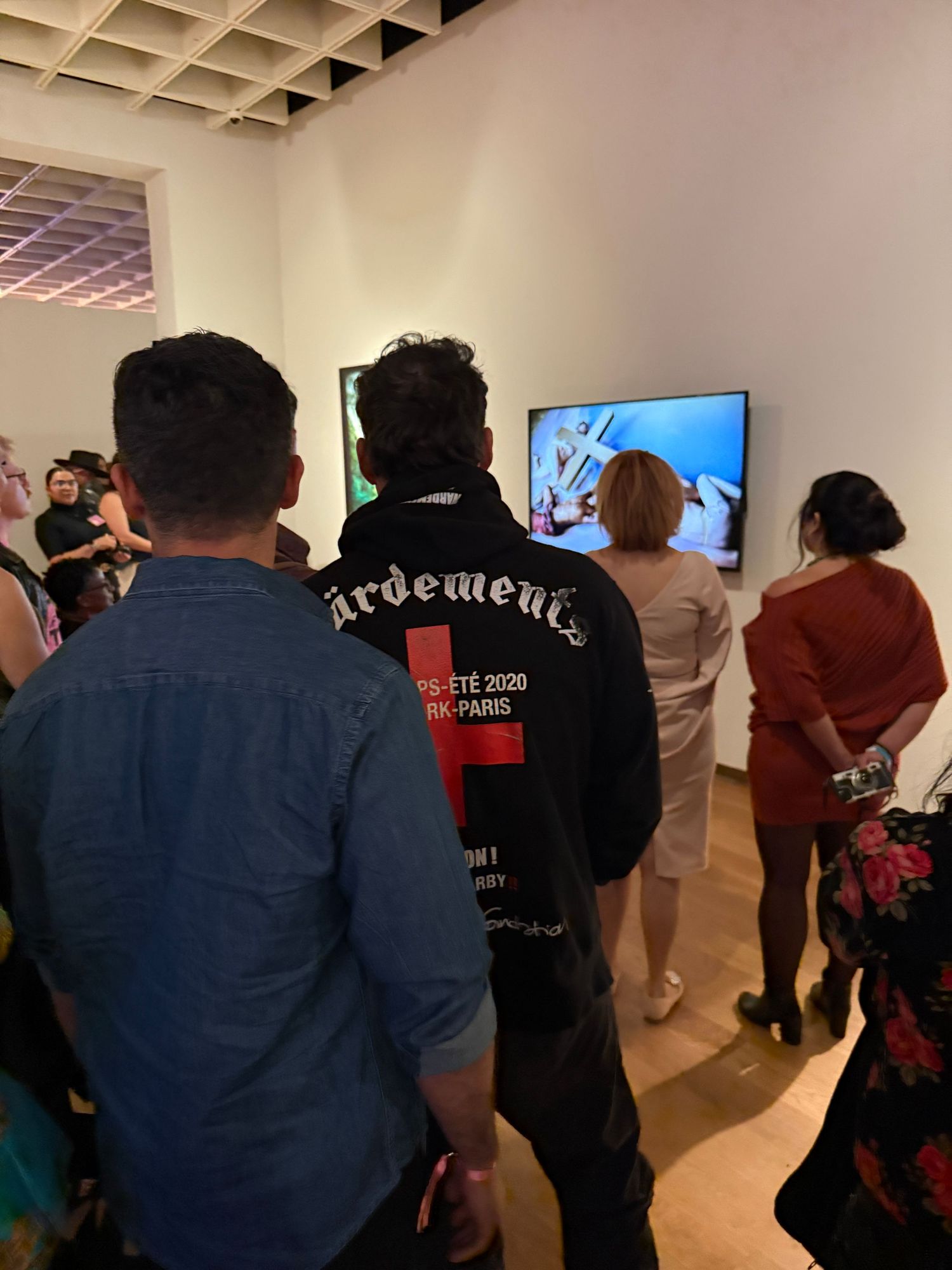 A group of people stand together viewing a wall-mounted display in a gallery or exhibition space.