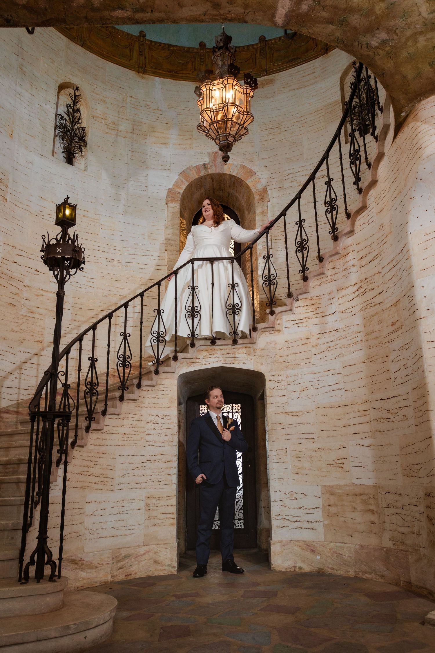 Bride and groom sharing a first look on an ornate spiral staircase in a historic stone mansion.
