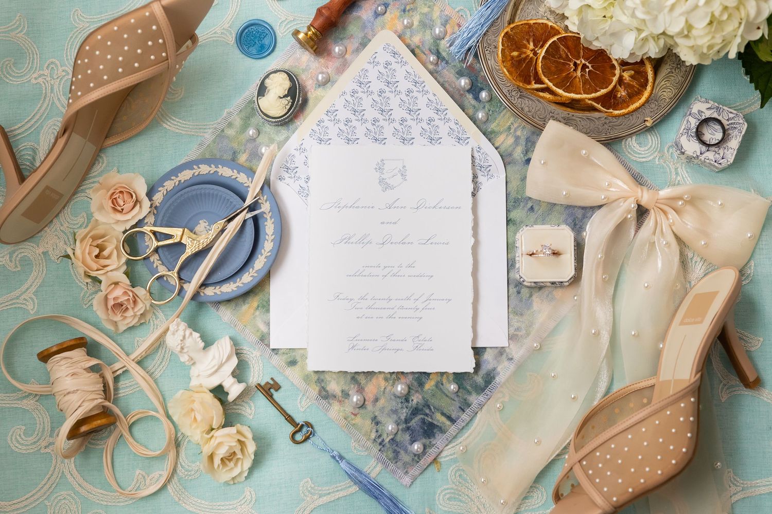Wedding stationery layout with vintage accessories and roses on blue background.
