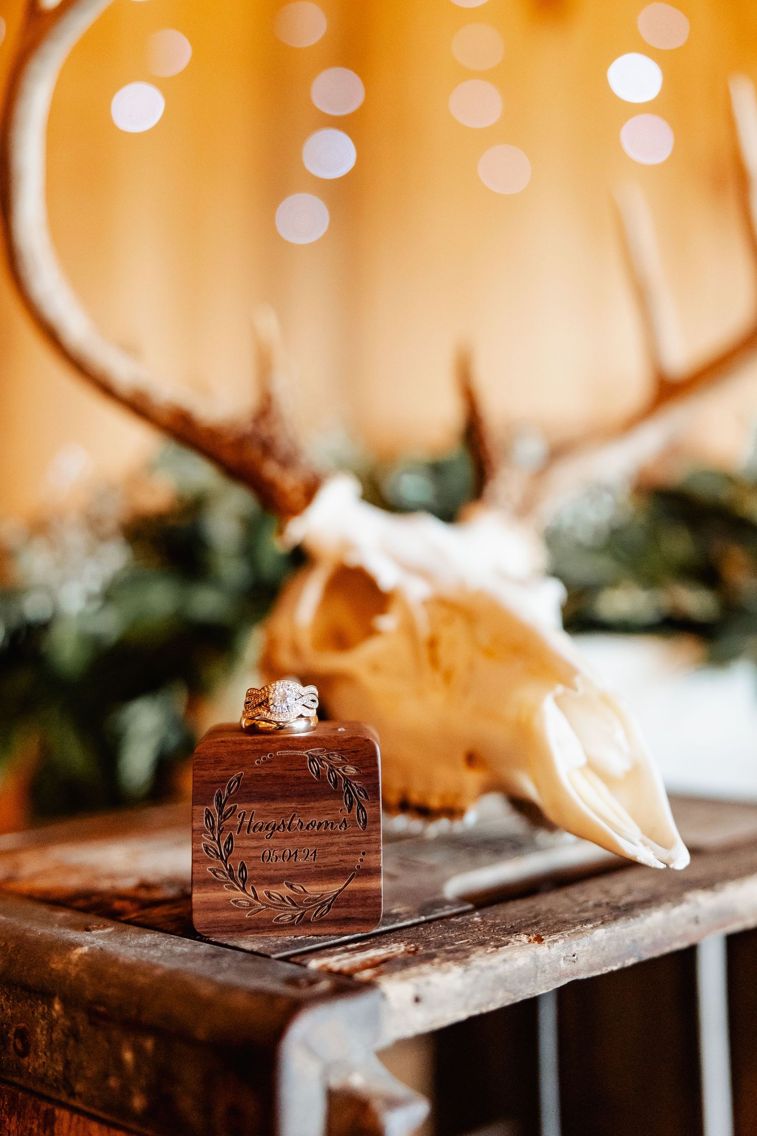 Wooden engraved perfume bottle with deer skull decor and string lights in background.