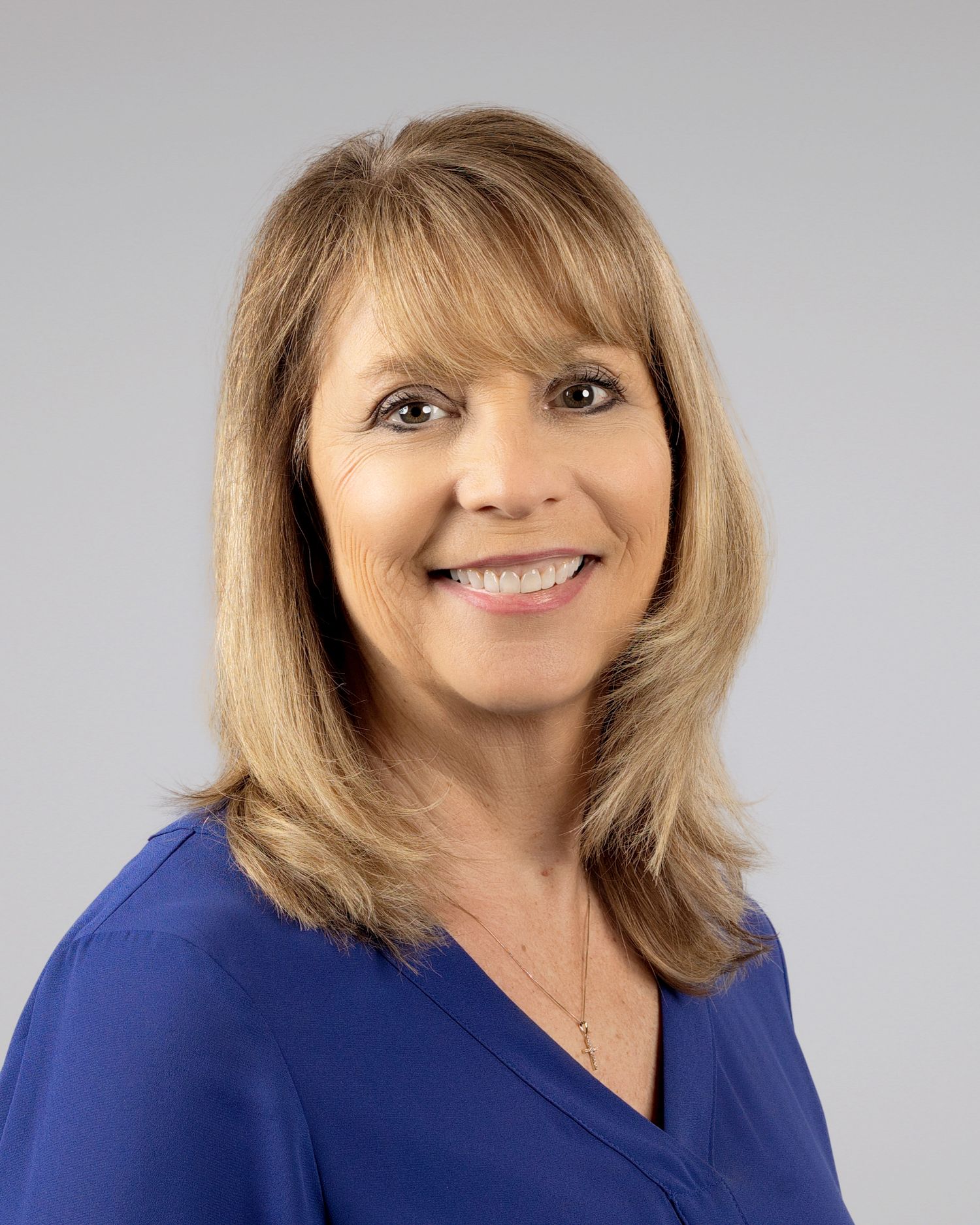 Friendly woman with medium blonde hair wearing a blue top smiles warmly in a professional portrait photo.
