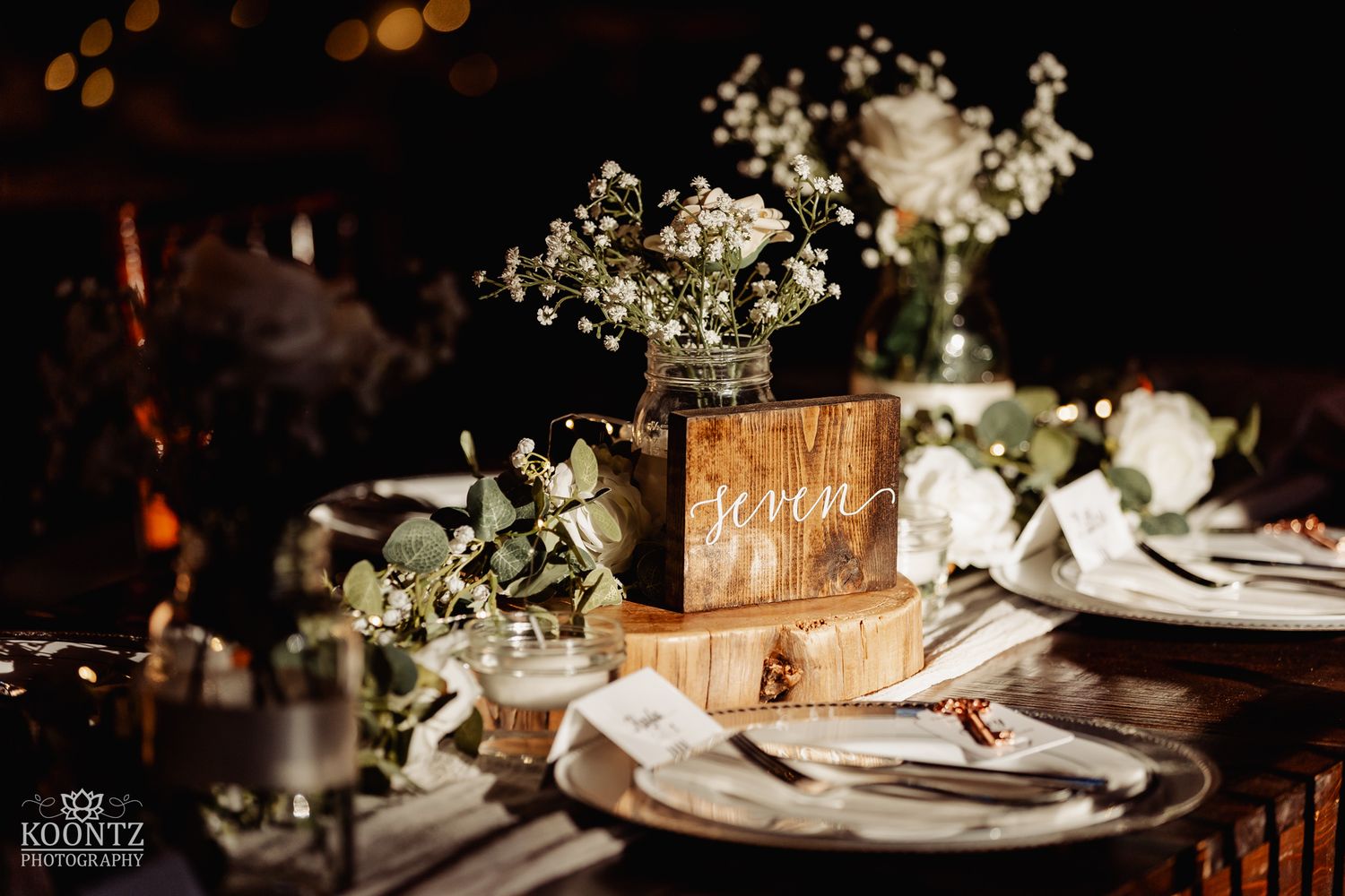 Rustic wooden table centerpiece with baby's breath in mason jar and calligraphy name card at reception.