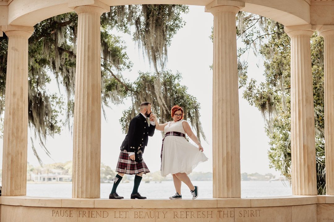 Bride and groom dancing joyfully under a classical columned pavilion with Spanish moss and waterfront views.