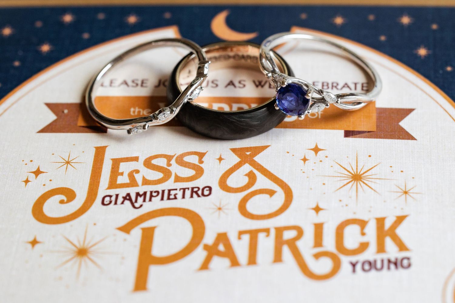 Wedding rings displayed on invitation card featuring Jess Giampietro and Patrick Young celestial design.