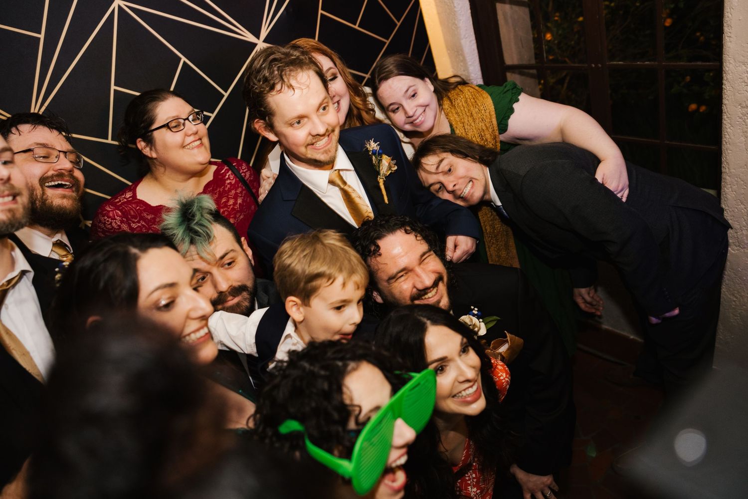 Groom surrounded by smiling wedding guests taking fun group photo at reception celebration.