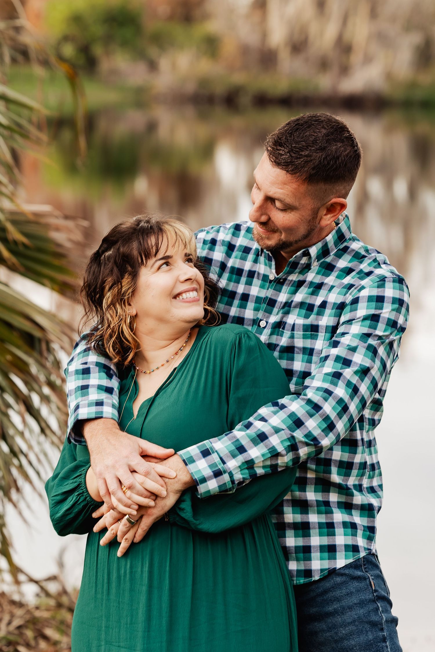 Romantic couple sharing a loving glance outdoors, woman in green dress embraced by man in plaid shirt.