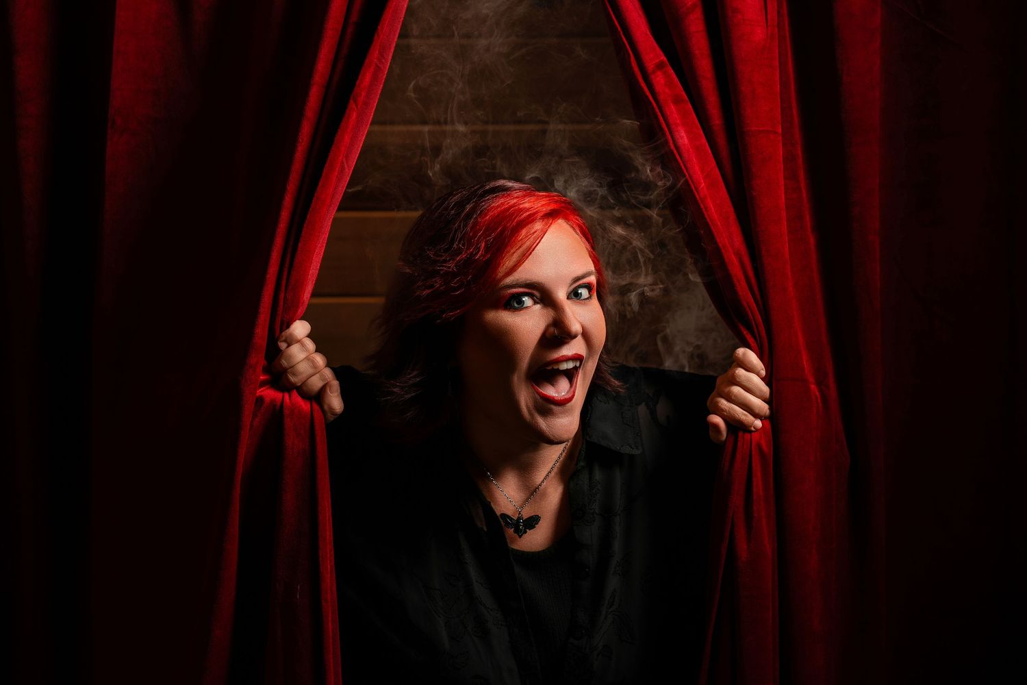 Woman with red hair dramatically parting red stage curtains with an expressive open-mouthed pose.