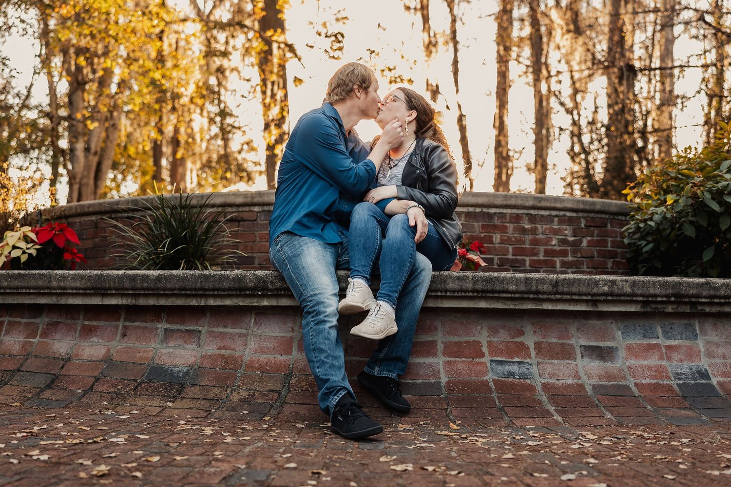 Couple sharing a tender kiss while sitting on a brick garden wall in autumn.