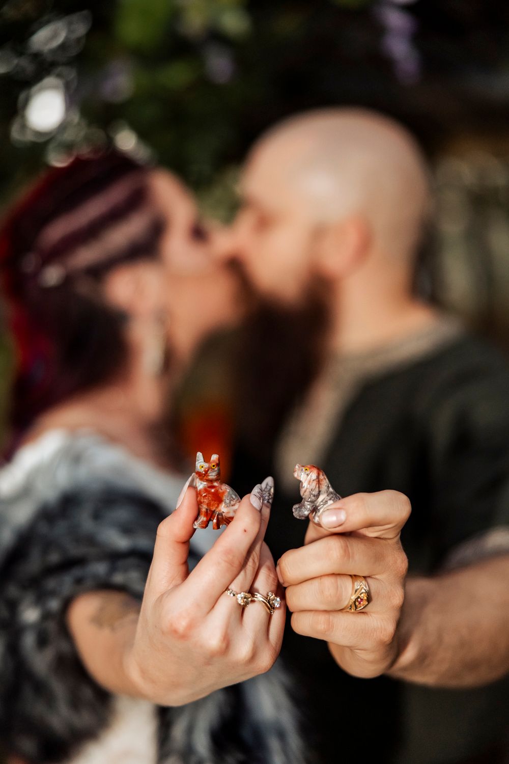 Viking wedding couple kisses while holding small fox figurines with ornate rings visible in foreground.