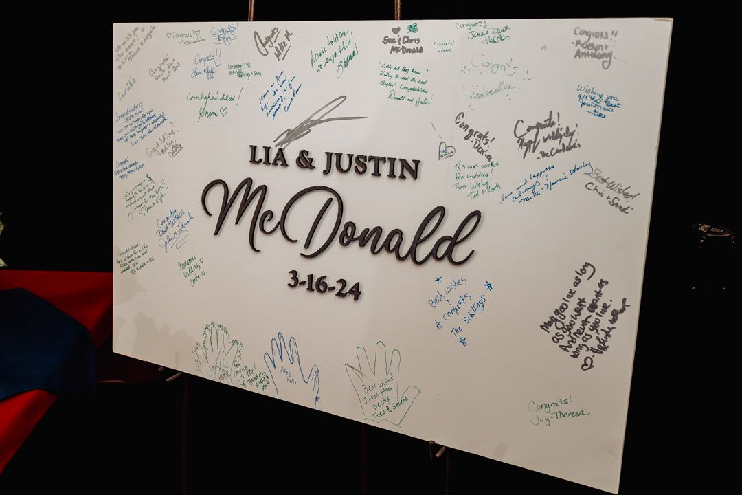 Wedding guest book signing board with names and date.