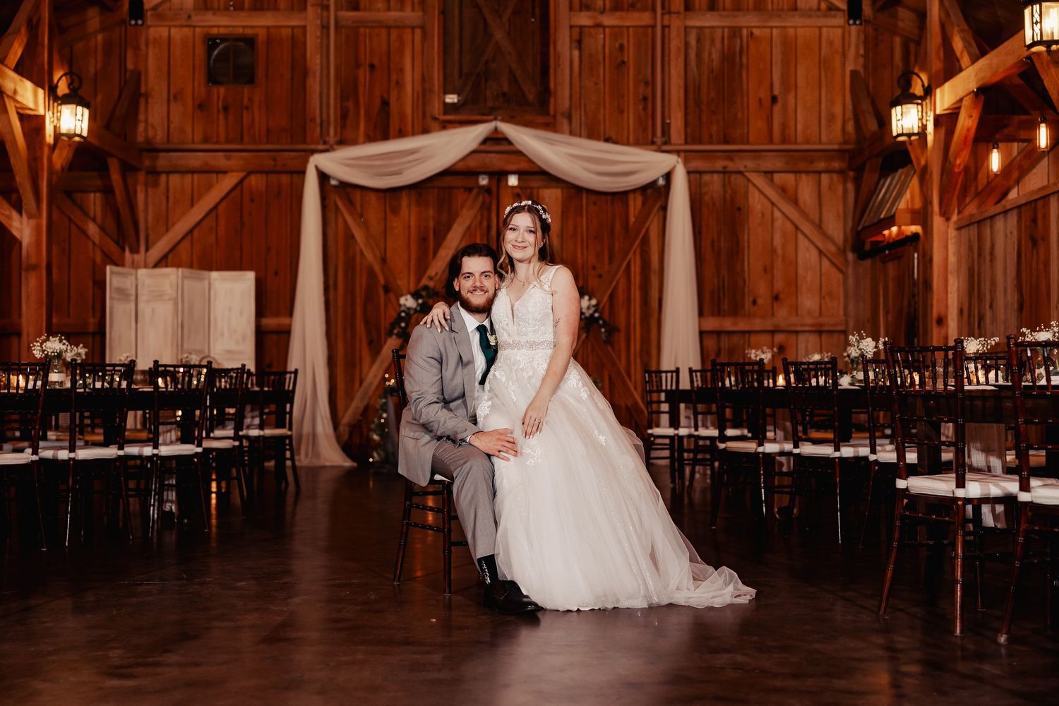 Elegant barn wedding ceremony setup with fabric draped arch and rows of chairs.