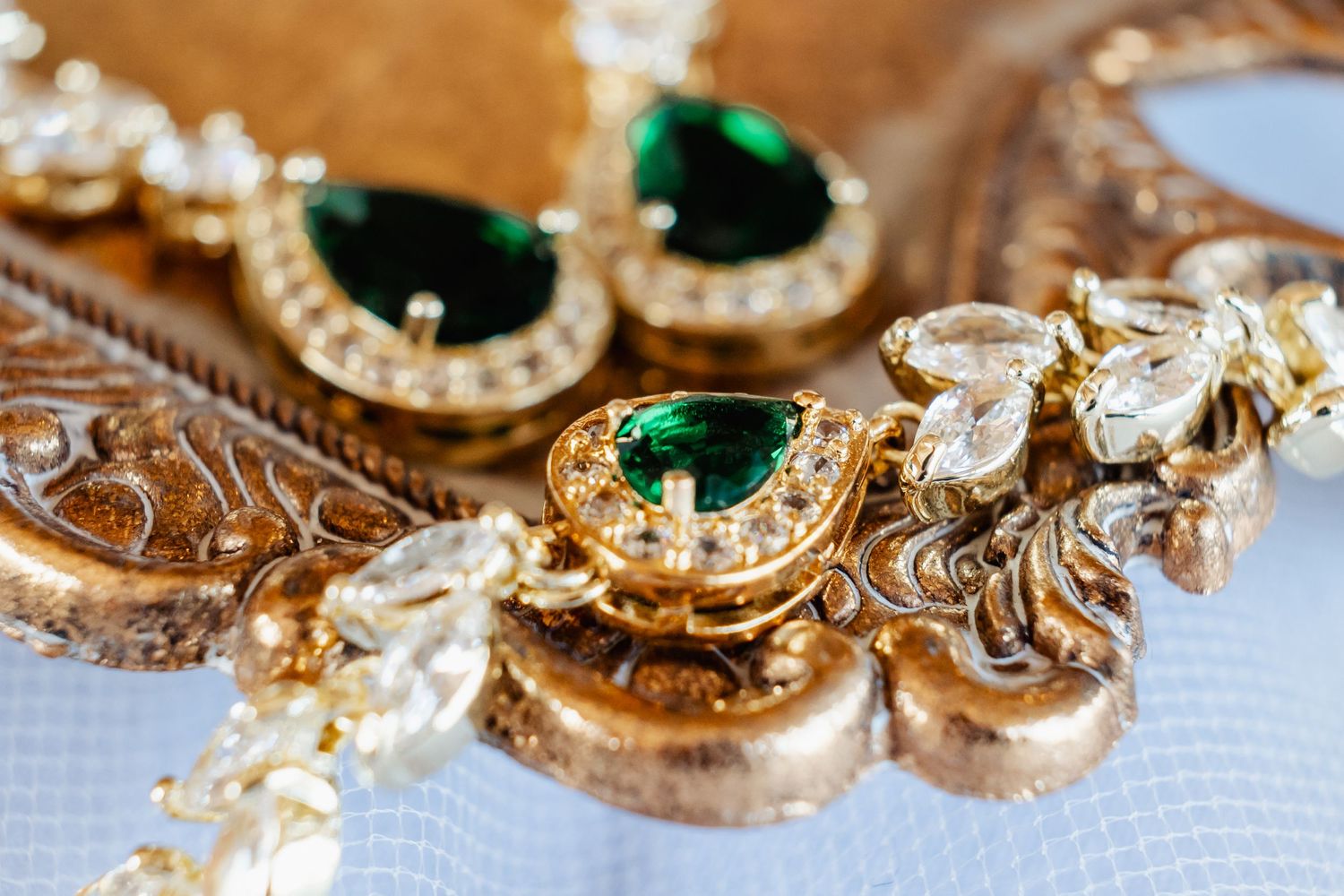 Vintage-style emerald and diamond jewelry pieces on ornate gold surface.