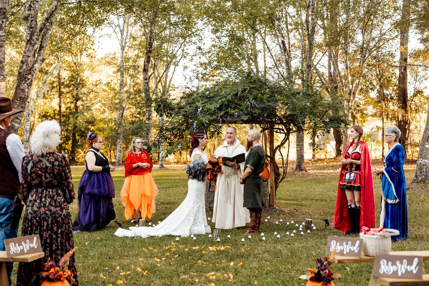 Outdoor medieval wedding ceremony with guests in colorful period costumes under autumn trees.
