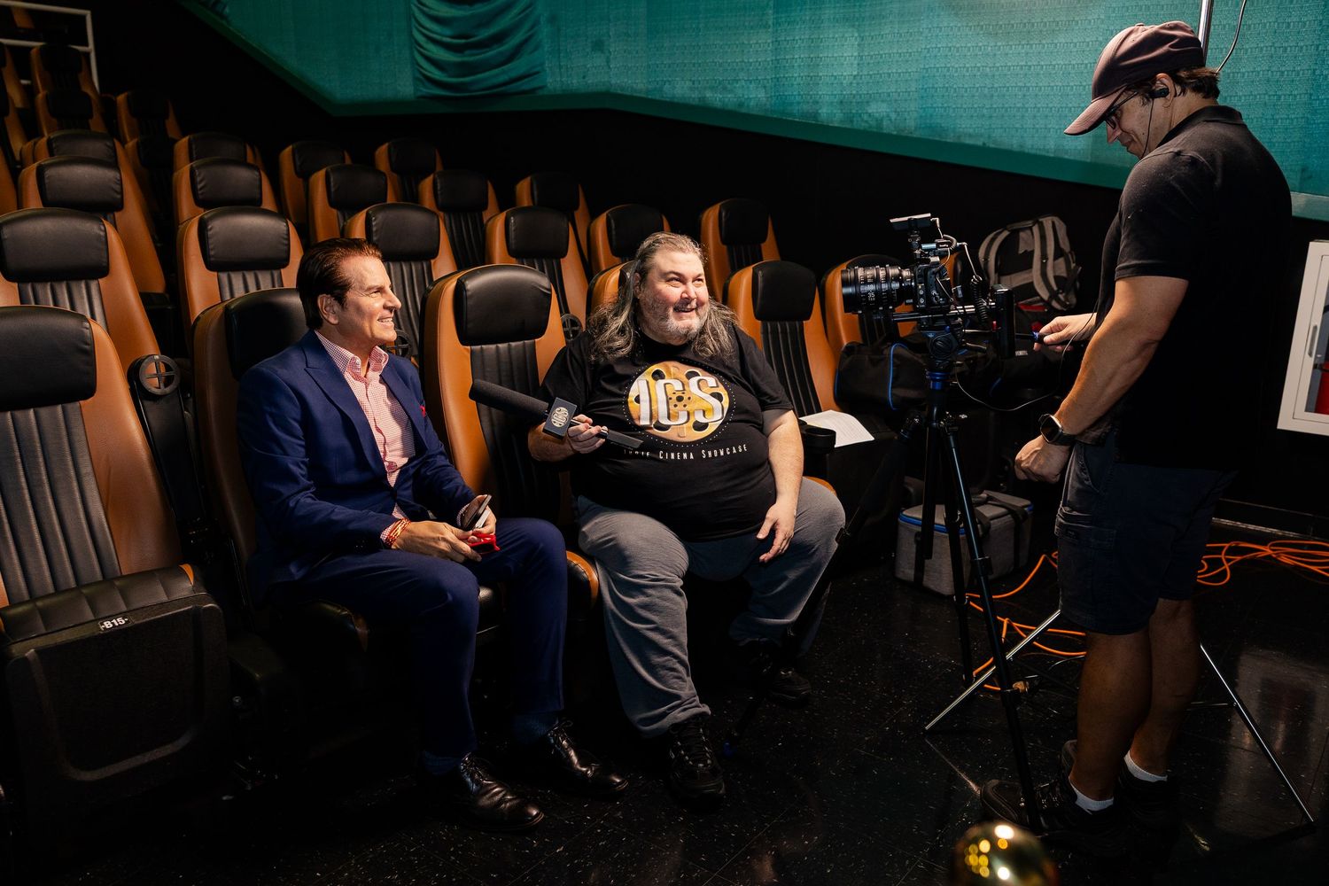 Behind-the-scenes interview filming inside a cinema with camera crew and two seated men.