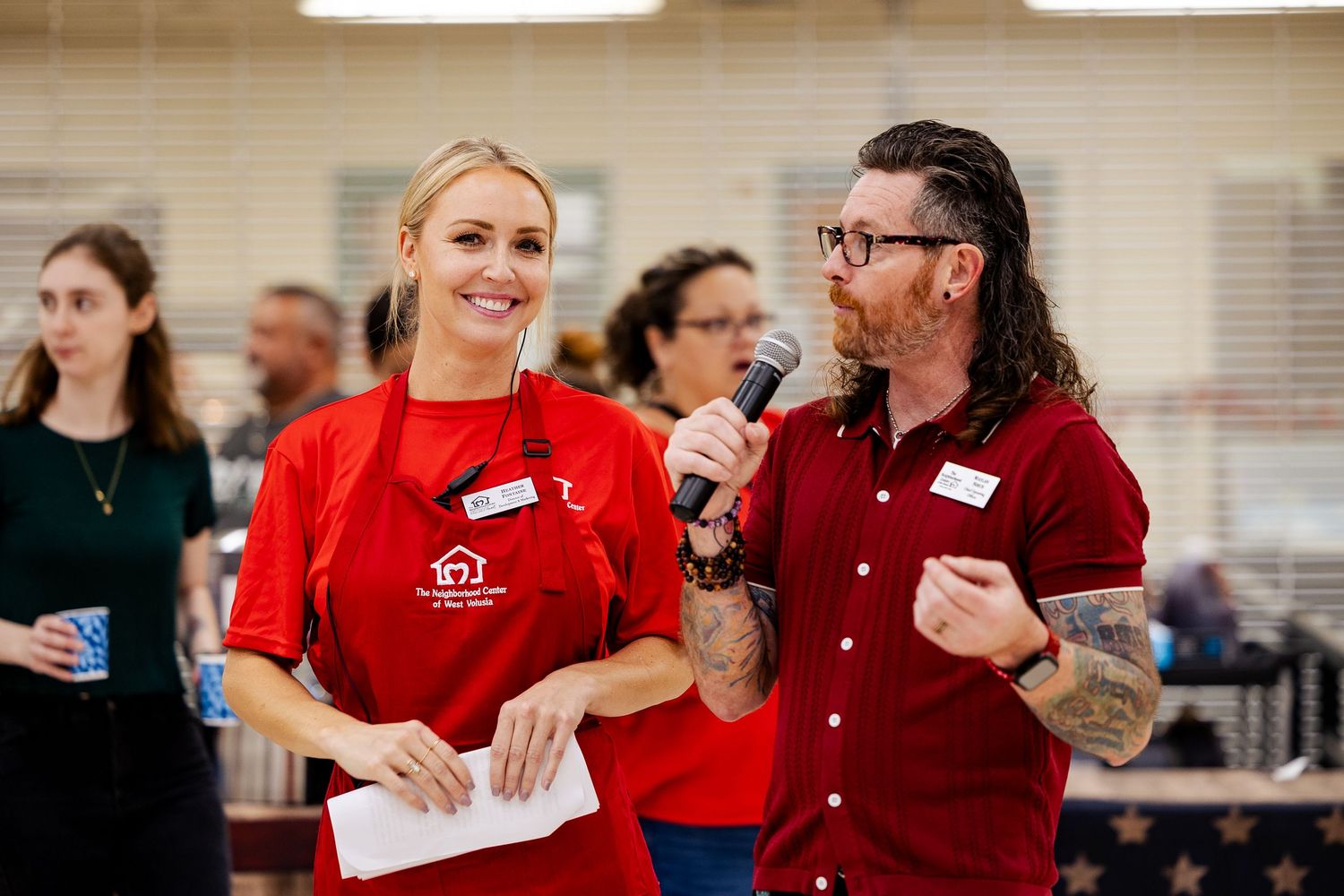 A man and woman in red attire share a microphone while hosting a community fundraising event.