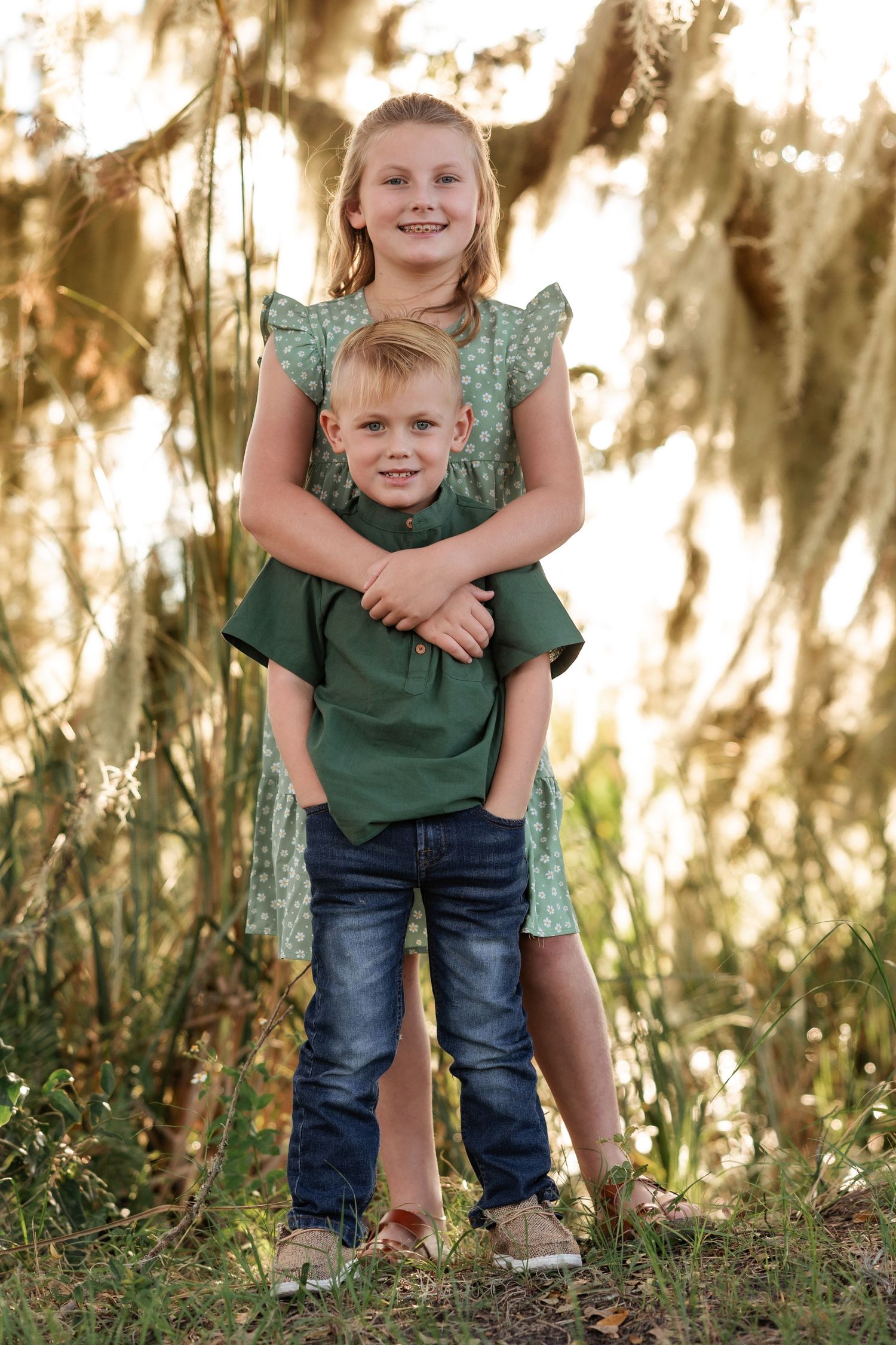 Two children embrace while posing outdoors under hanging Spanish moss.