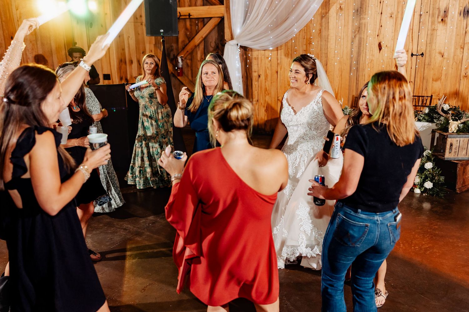 Wedding party dances enthusiastically on wooden dance floor during barn reception.