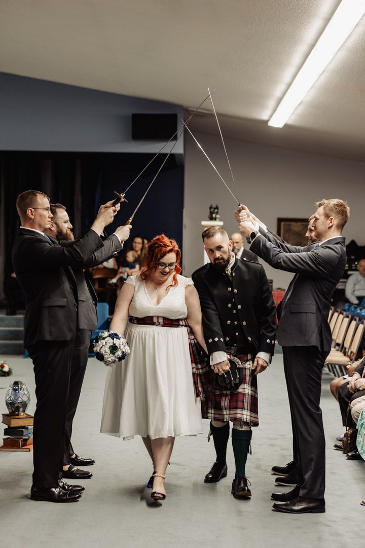 A wedding party holds ceremonial swords in an arch formation during an indoor celebration.