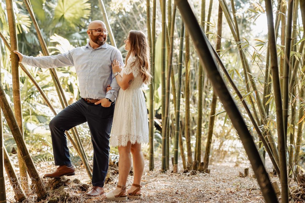 A couple poses playfully among tall bamboo stalks in a tropical garden setting.