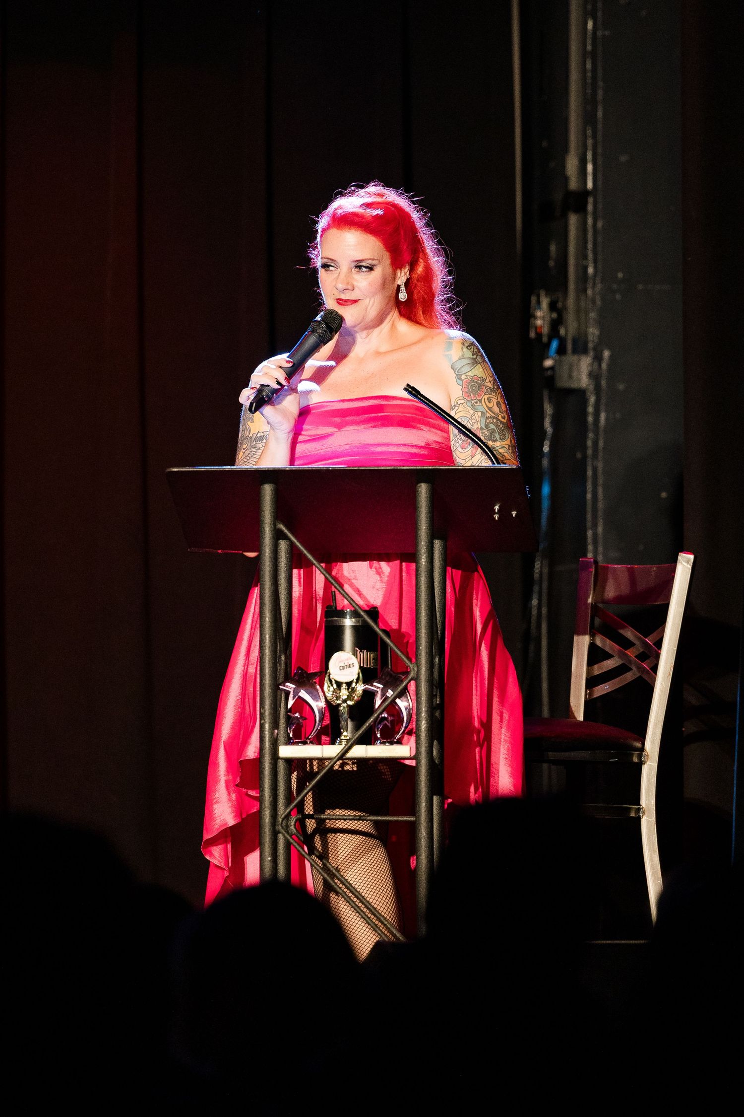 Red-haired woman in pink strapless gown speaking at podium with microphone on stage.