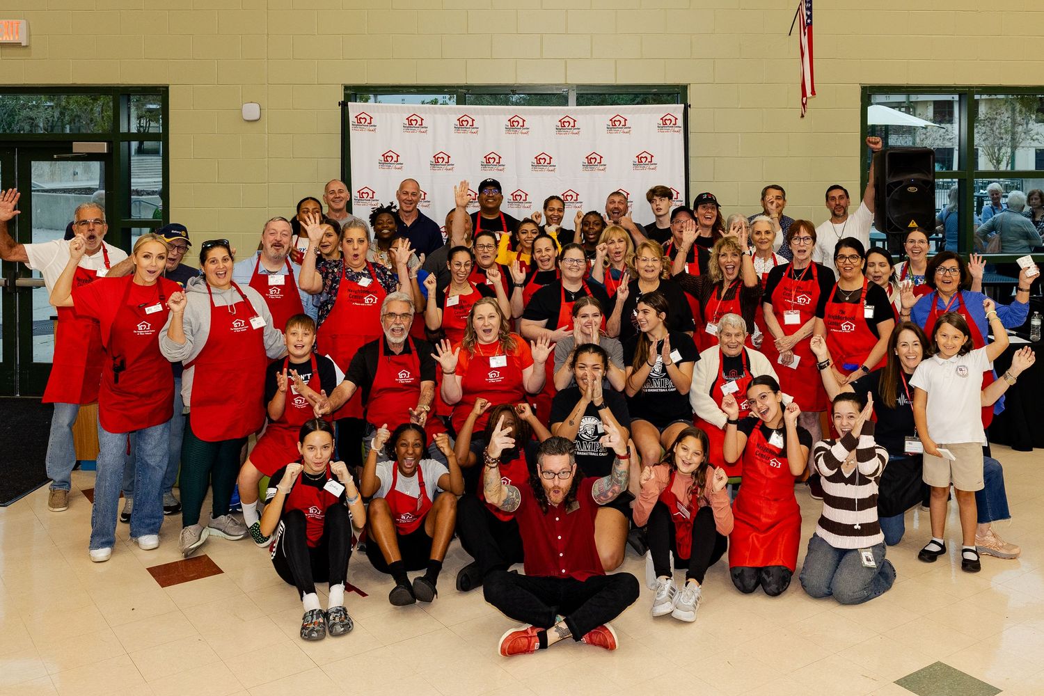 Large group of cheerful volunteers in red aprons making fun gestures for a group photo.