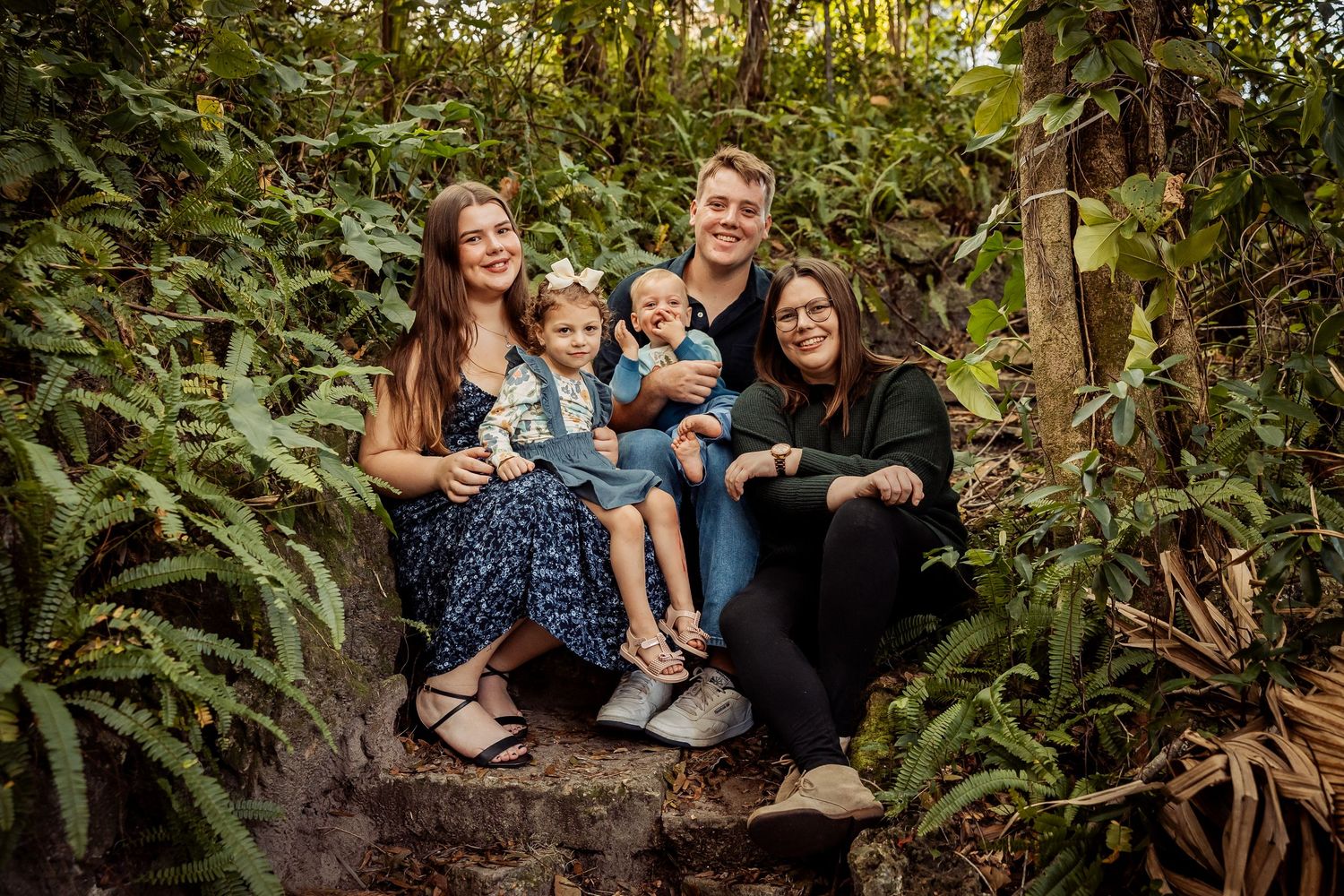 Family of five posing on stone steps surrounded by tropical greenery, including three young children.