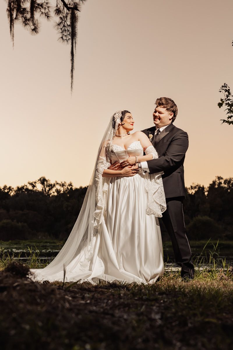 Bride and groom share a romantic embrace at golden hour beneath Spanish moss-draped trees.