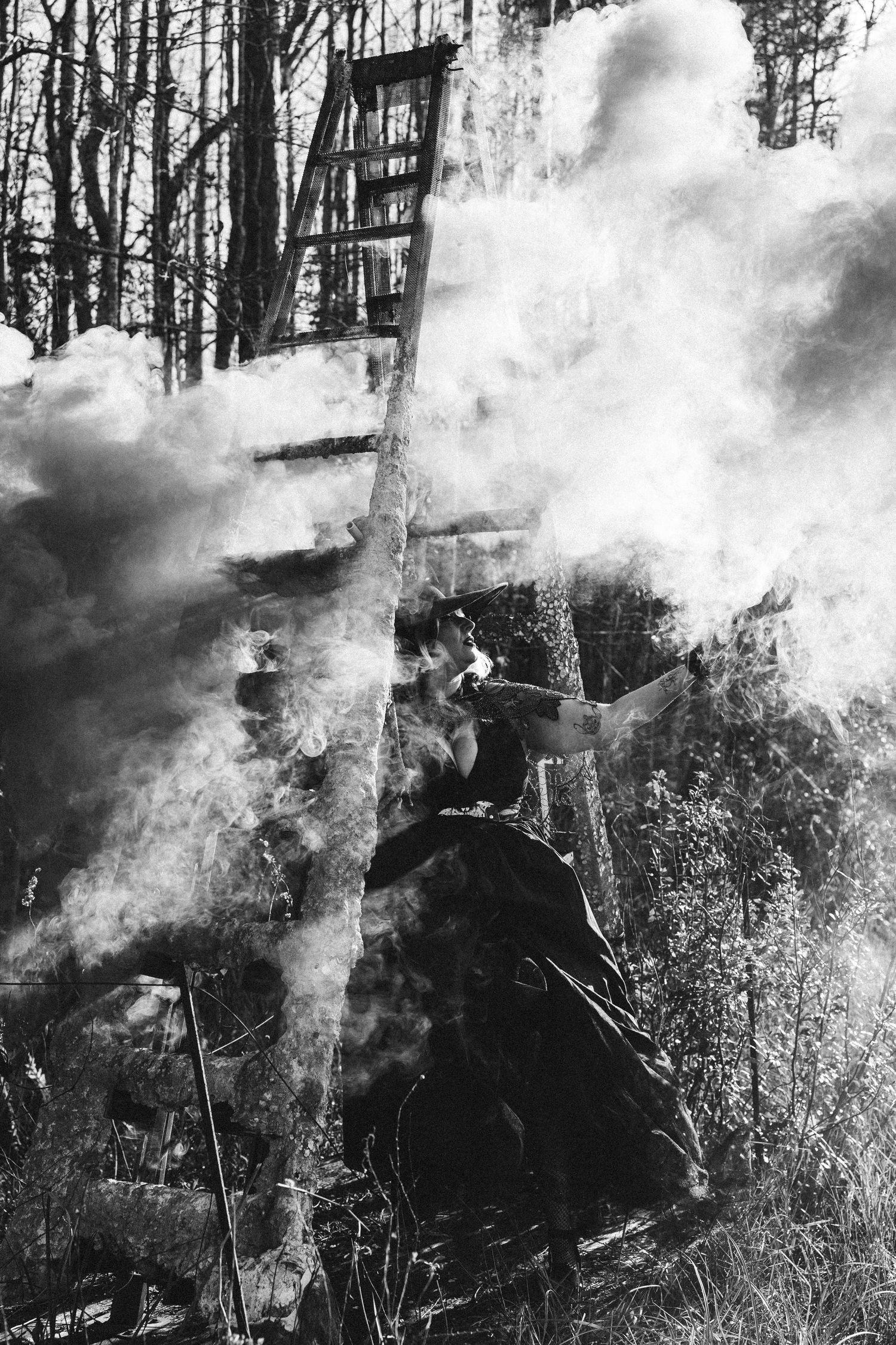 Black and white dramatic photo of figure amid billowing smoke near rustic wooden structure.