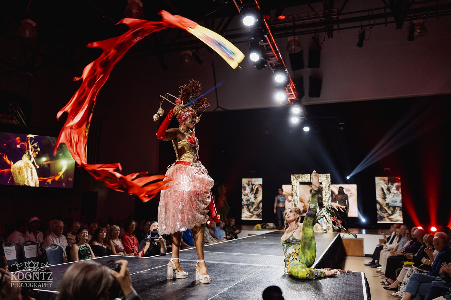 Contemporary dancers perform in red and black lighting on stage with expressive movements.