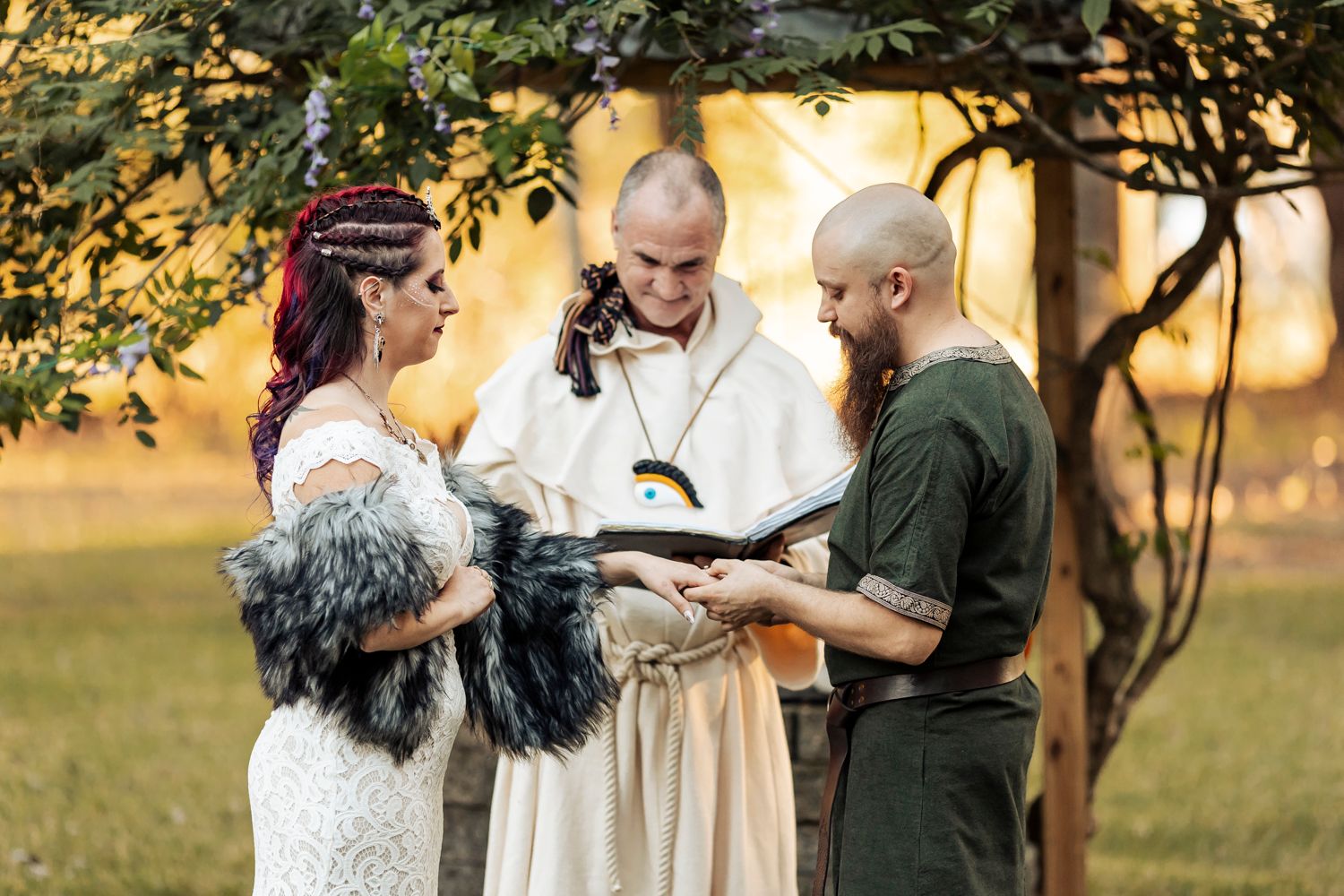 Medieval-style wedding ceremony with officiant in white robes reading from ceremonial book.