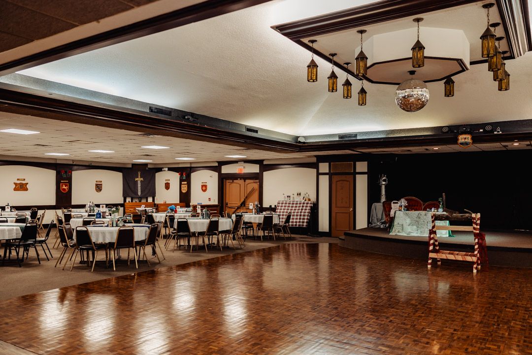 Elegant wedding reception hall with parquet dance floor, round tables, and hanging lanterns.