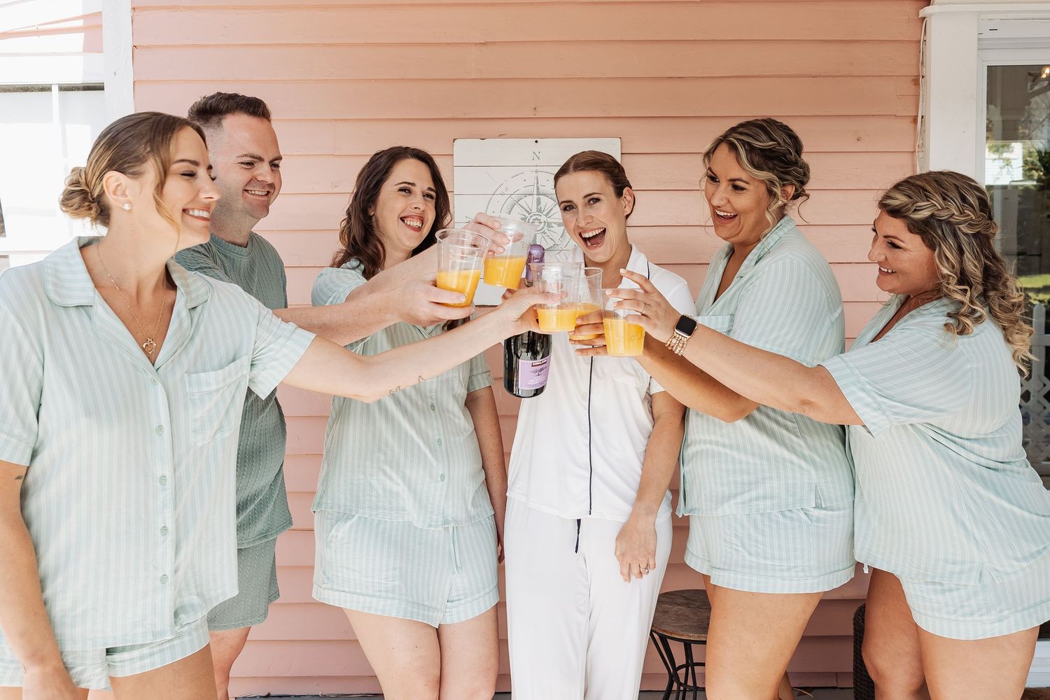 Bridal party in matching mint pajamas toasting with orange juice drinks before the wedding.