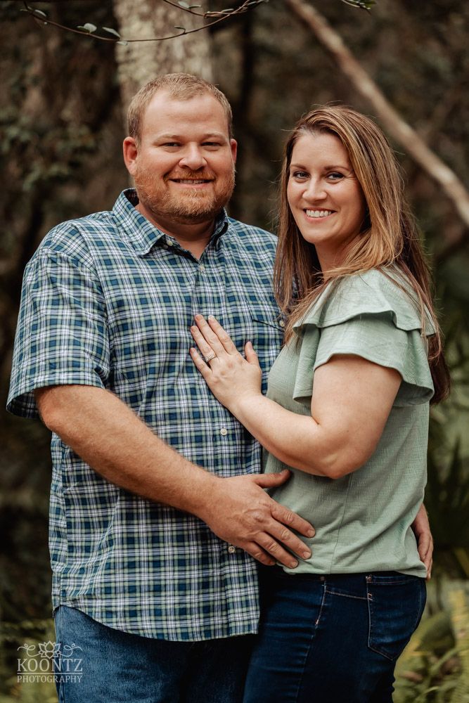 Couple in casual attire embracing outdoors with a natural wooded background.