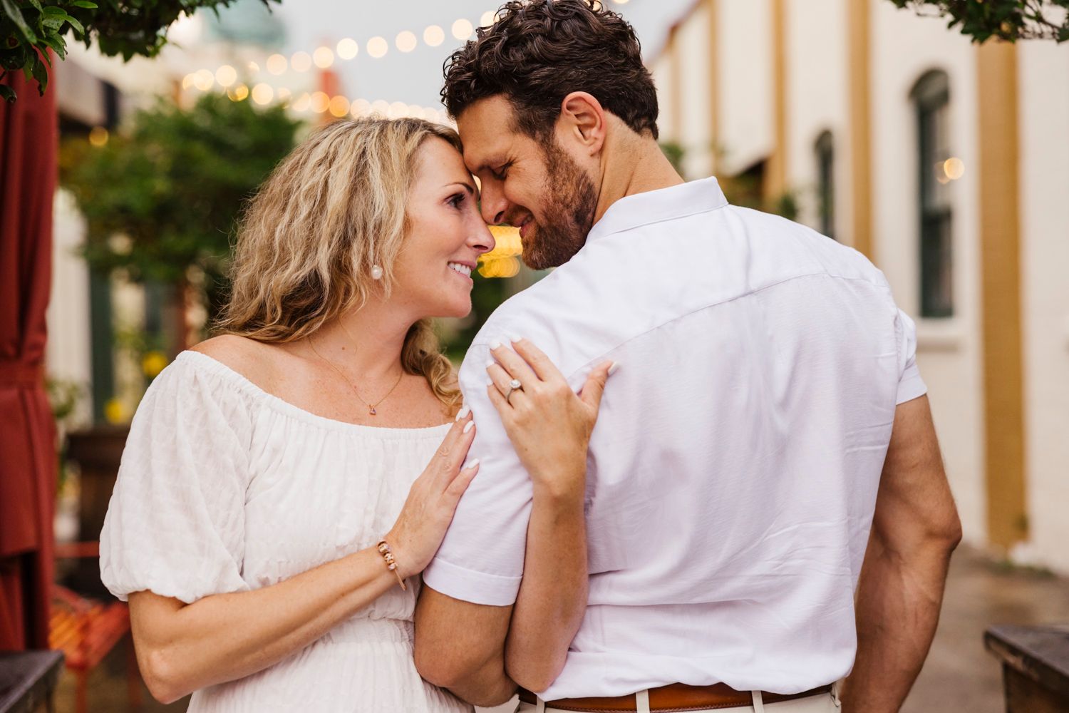 Romantic couple sharing an intimate moment in front of a colorful building with string lights.