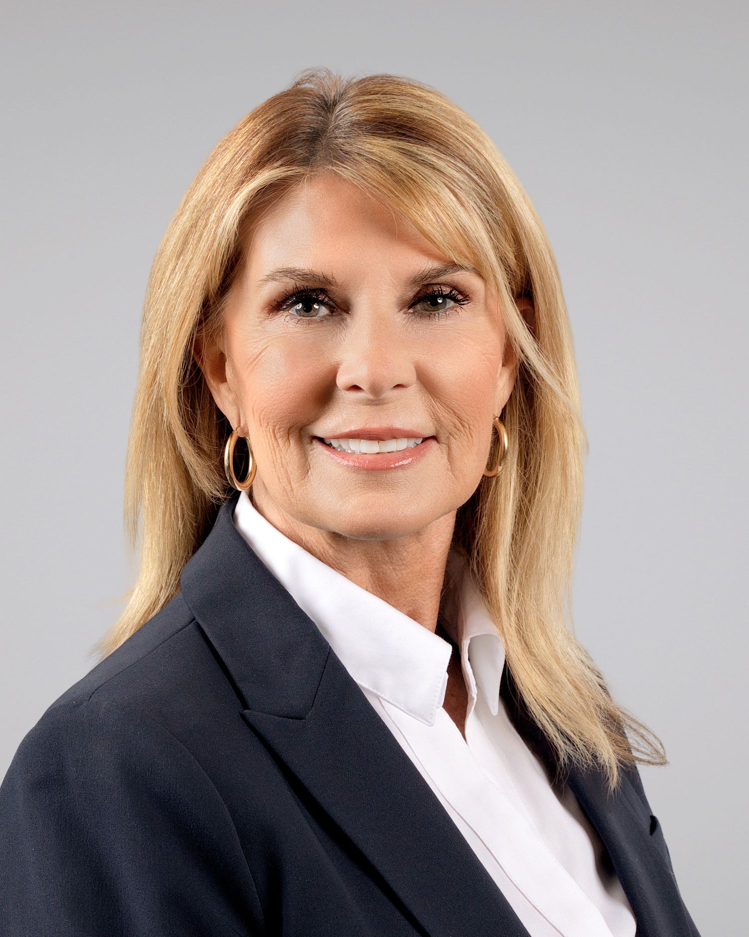 Professional woman with blonde hair wearing a navy blazer and white shirt smiles for a corporate headshot.