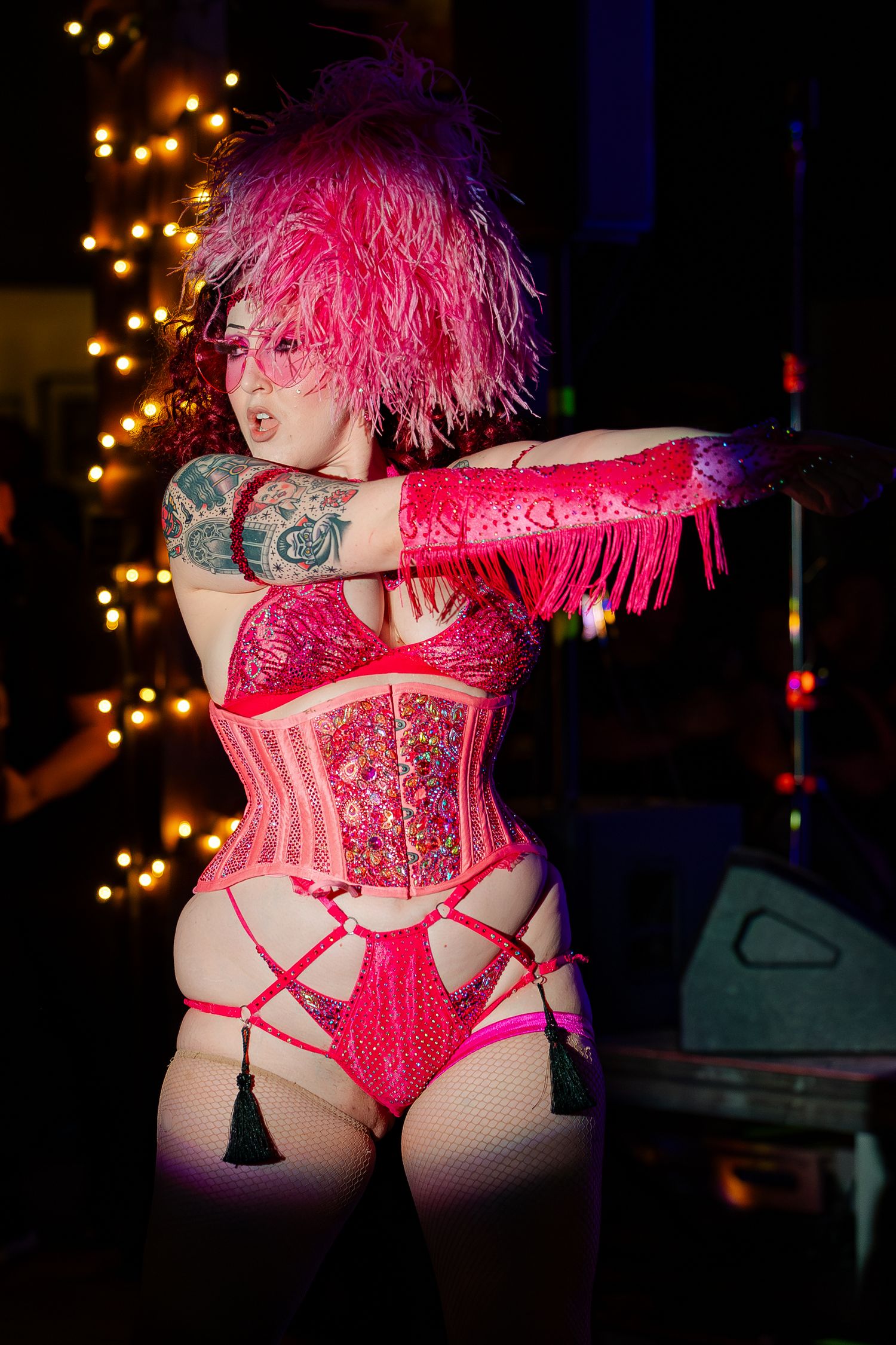 Burlesque performer in pink feathered headpiece and red corset costume posing under warm stage lights.