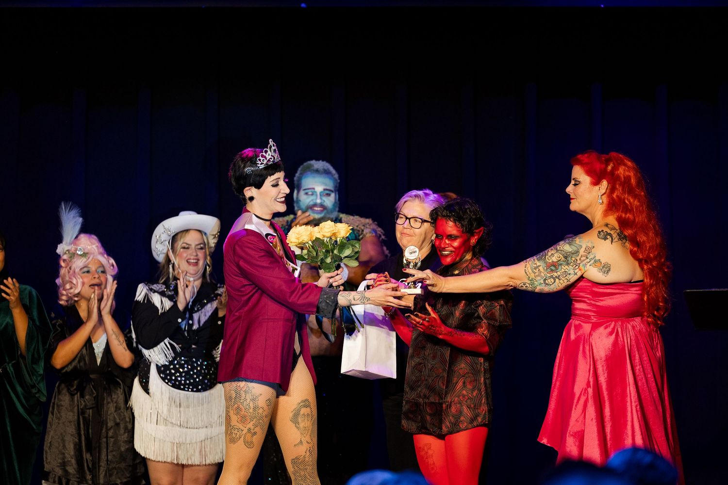 Burlesque performers gather on stage as a winner receives flowers during a competition finale.