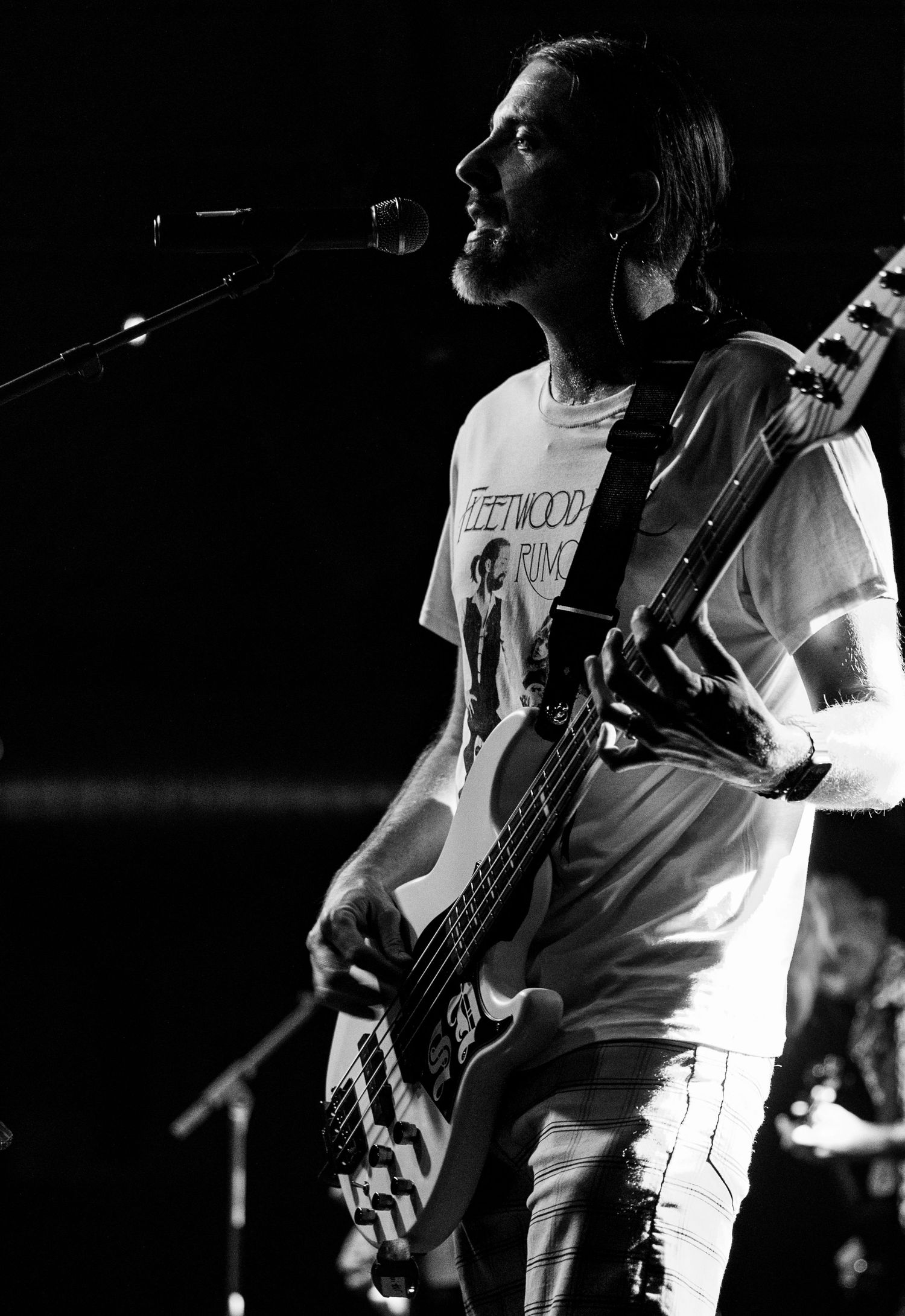 Bass guitarist performing on stage in black and white wearing a Fleetwood Mac t-shirt.