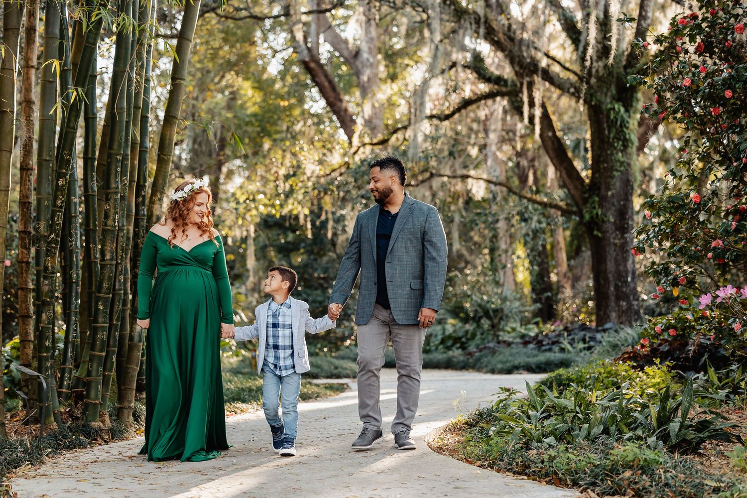 Family walking together on garden path, pregnant mother in elegant green maternity gown.