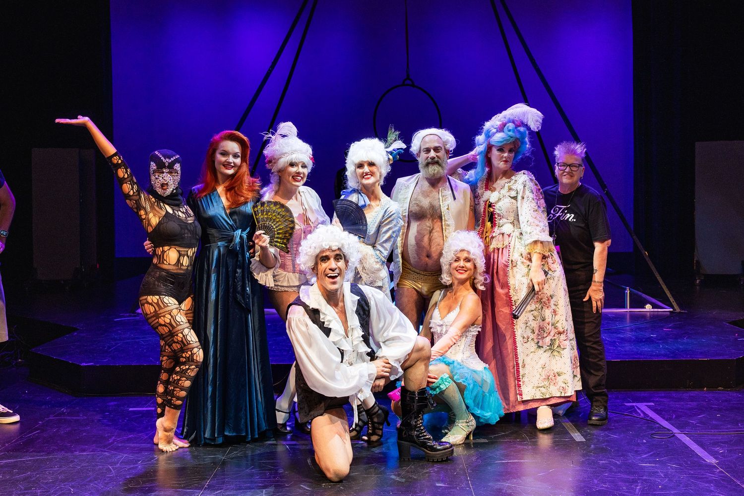 Diverse burlesque cast in colorful costumes pose together for group photo on stage after performance.