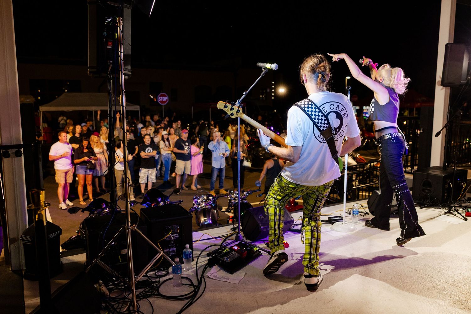 Rock band performs on outdoor stage to large crowd gathered at night concert.