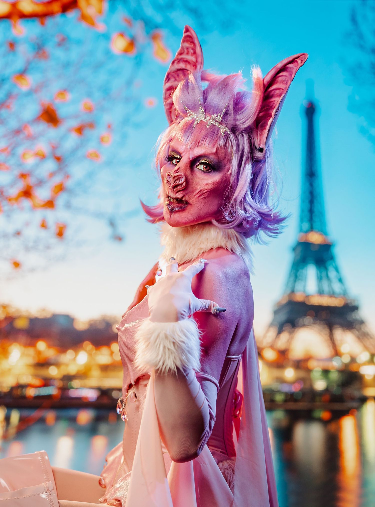 Person in pink demon costume with horns poses in front of the Eiffel Tower at twilight in Paris.