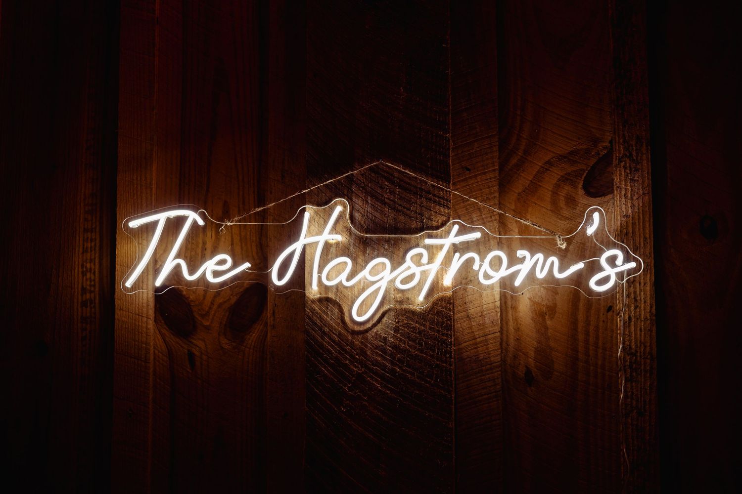 Illuminated neon sign reading 'The Hagstrom's' mounted on wooden wall.